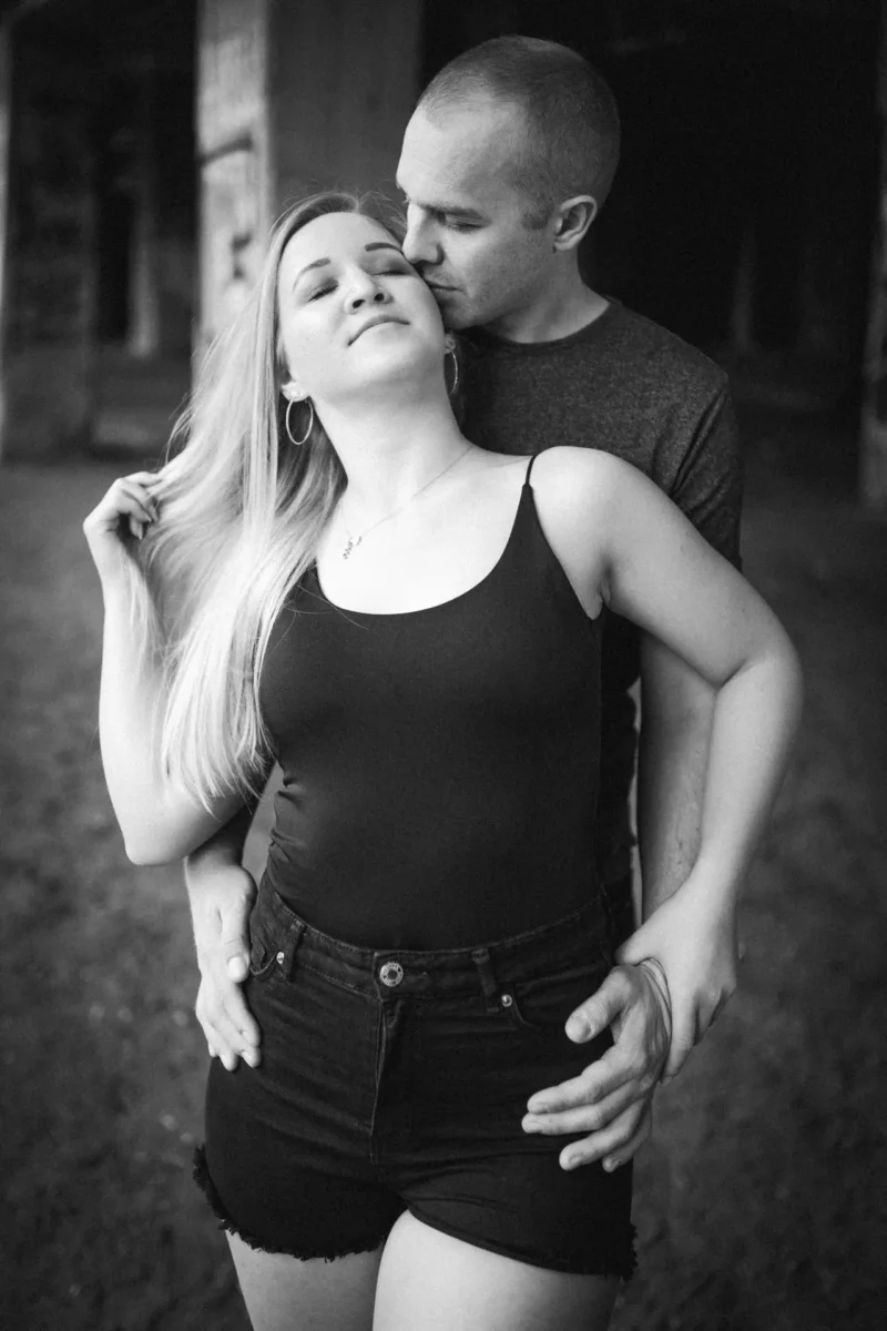 Laura und Emilis - Urbane Location in Plagwitz Paarfotograf Leipzig urban – Schwarzweißportrait Paar unter Brücke, Mann küsst Frau auf die Wange