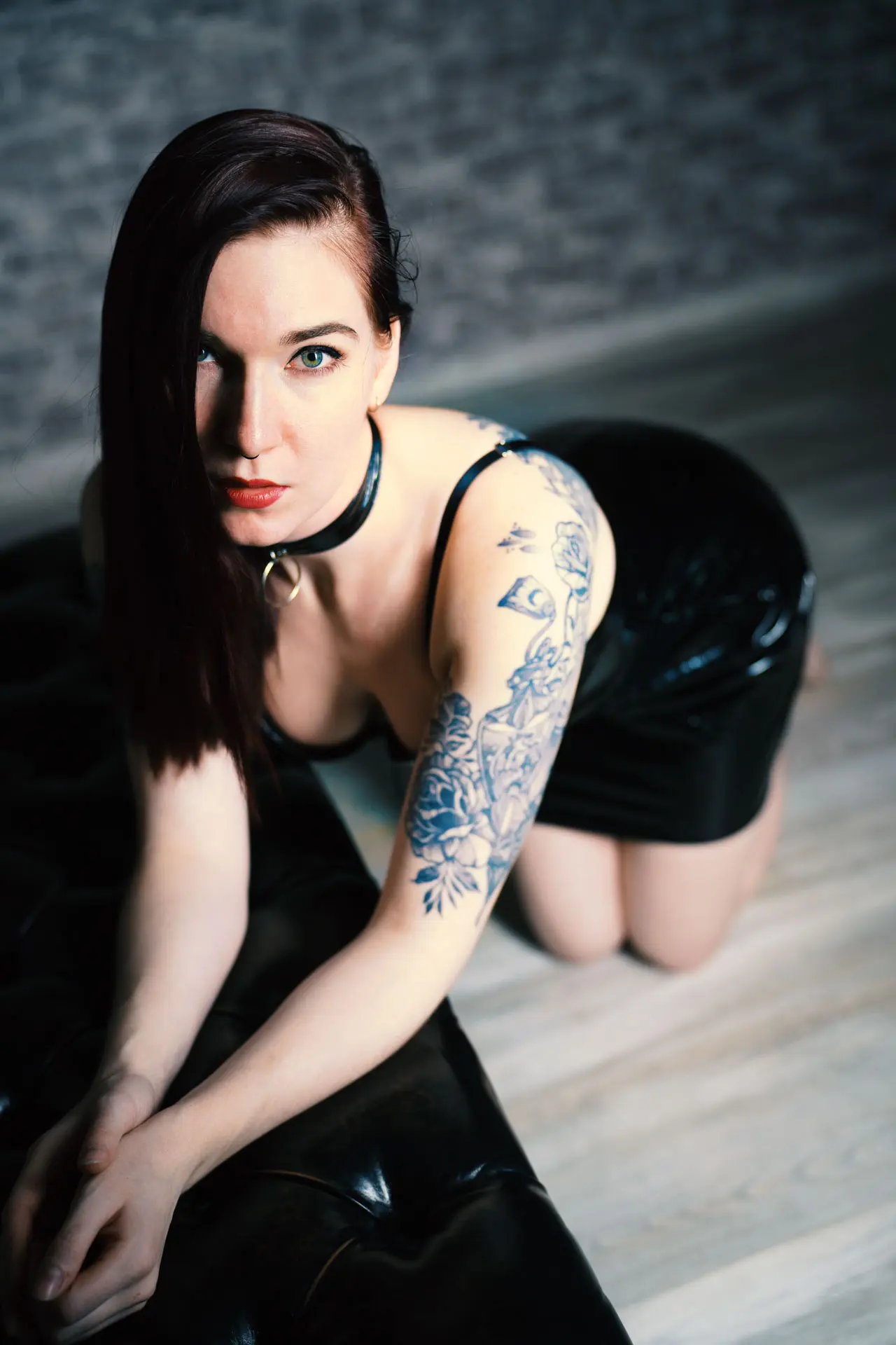 Frau im schwarzen Latexkleid mit Halsband kniet auf dem Boden und blickt intensiv in die Kamera – Kinky Boudoir Fotoshooting Leipzig