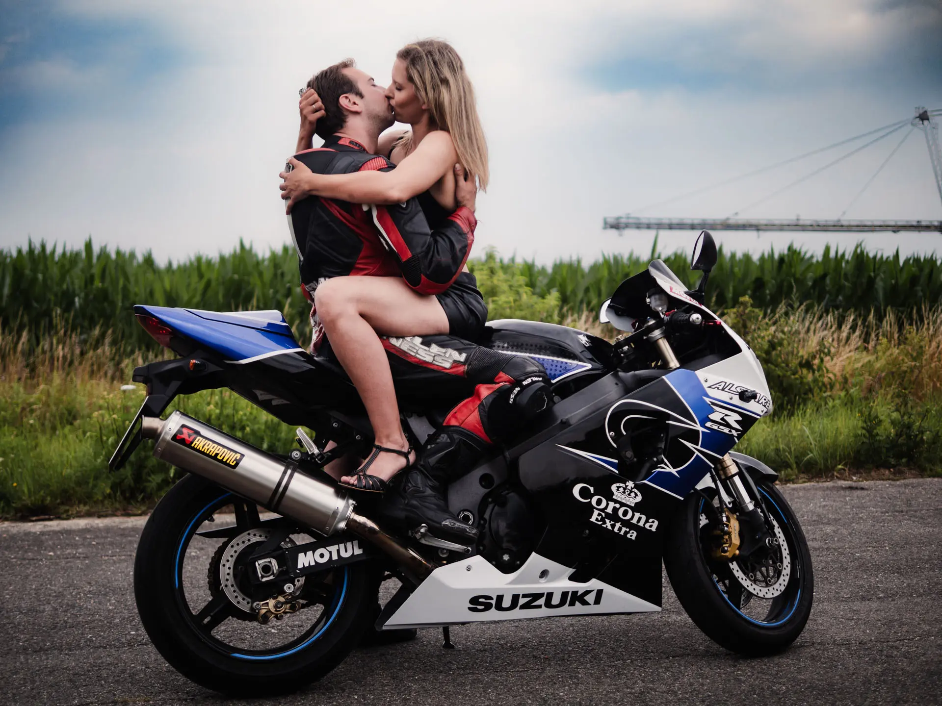 Küssendes Paar auf Suzuki Motorrad, er in Lederkluft, sie in sexy Ledershorts auf seinem Schoß sitzend