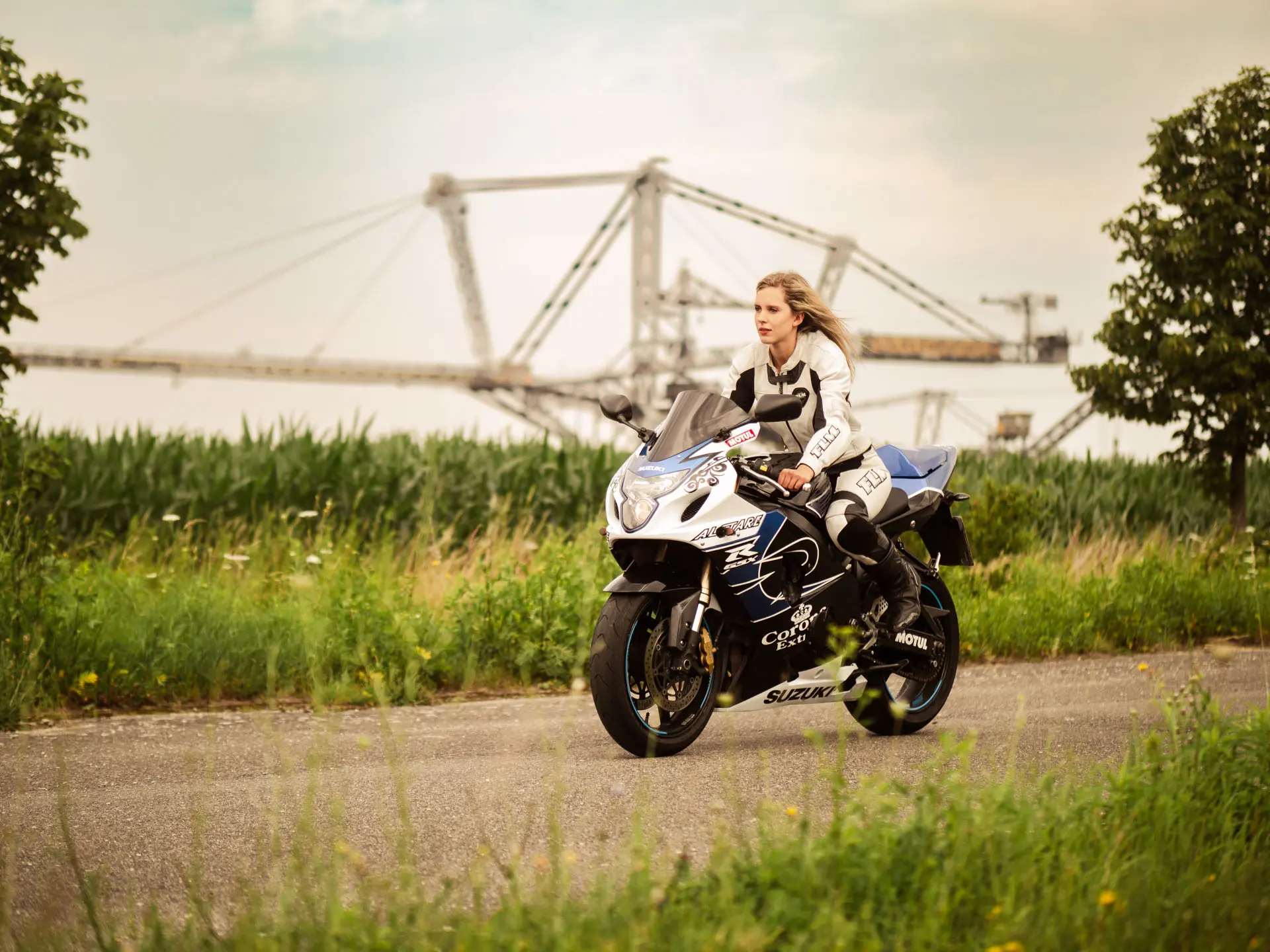 Frau in Motorrad-Lederkombi auf Suzuki Sportbike, Industriekulisse im Hintergrund