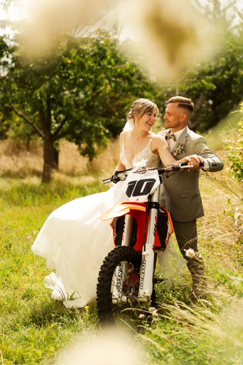 Hochzeitspaar mit Motocross-Maschine im Grünen, Brautkleid am Motorrad