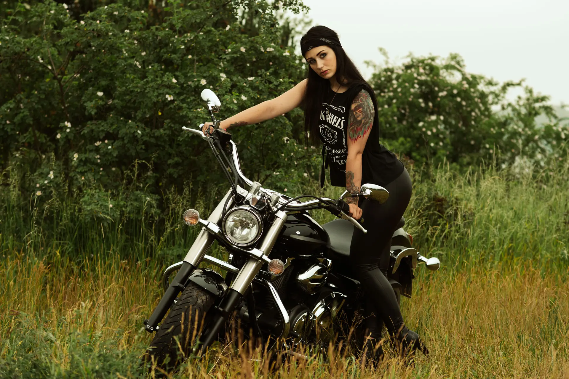 Tätowierte Frau im Bikerlook auf Yamaha Cruiser im hohen Gras