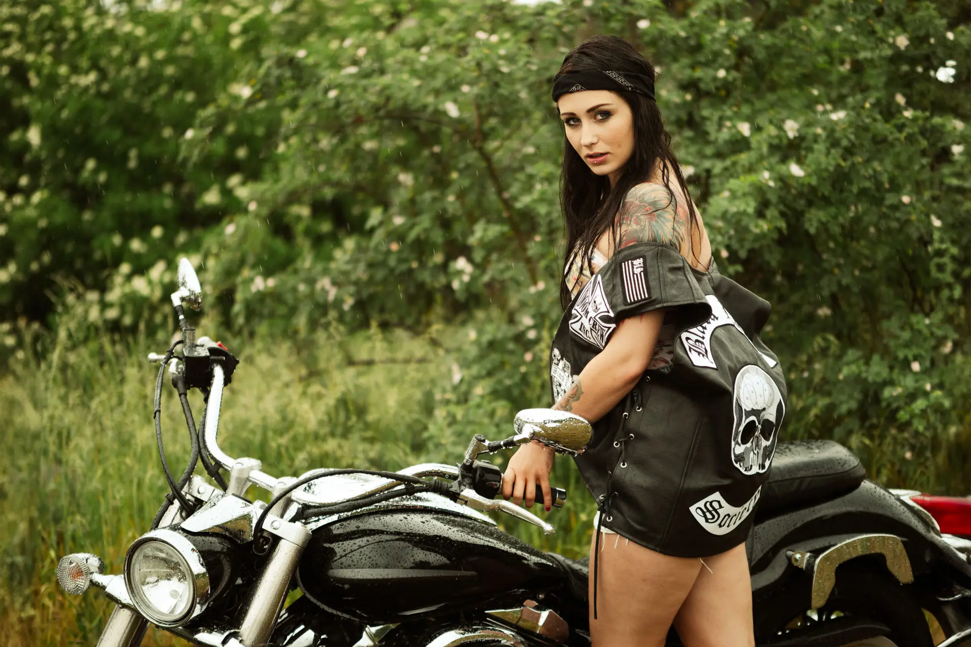 Bikerin mit Kutte und Totenkopf-Patch an Yamaha Cruiser im Regen