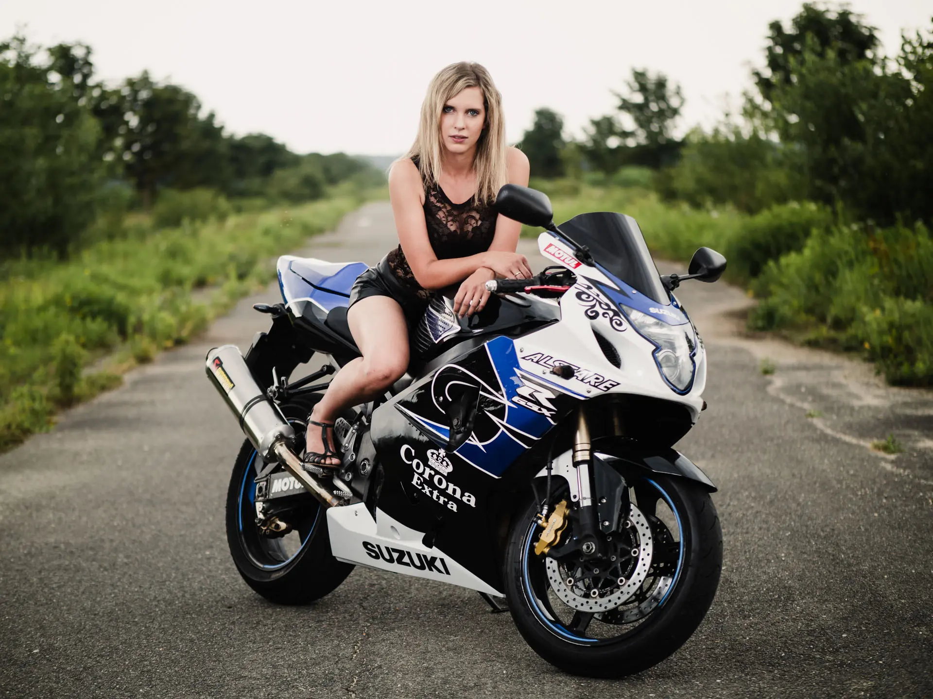 Frau in Spitzentop und Lederhose sitzt auf Suzuki Motorrad auf Landstraße